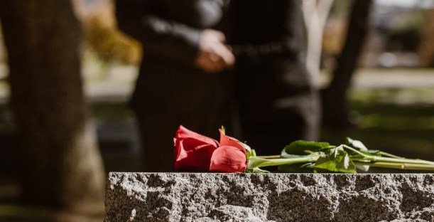 man and woman standing on grave with flower on tombstone